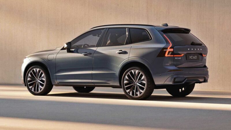 A gray Volvo XC60 SUV is parked on a smooth surface in front of a plain beige wall, shown from a rear side angle, as Volvo expands U.S. operations with XC60 production from 2026.