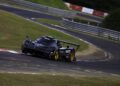 A black Pagani with gold wheels speeds along a winding racetrack surrounded by grass and guardrails during the 2025 Monterey Car Week car event.