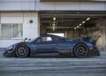 A black Pagani Zonda sports car is parked in front of a garage at a racetrack, viewed from the side—capturing the excitement of Monterey Car Week.