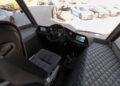 The interior of a compact vehicle with quilted upholstery, a single seat, steering wheel, digital displays, and a manual gear stick; like an Atlas ATV for sale, cars are visible through the windshield.