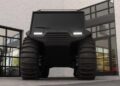 Large black Atlas ATV with oversized tires is parked in front of a modern building with glass garage doors.