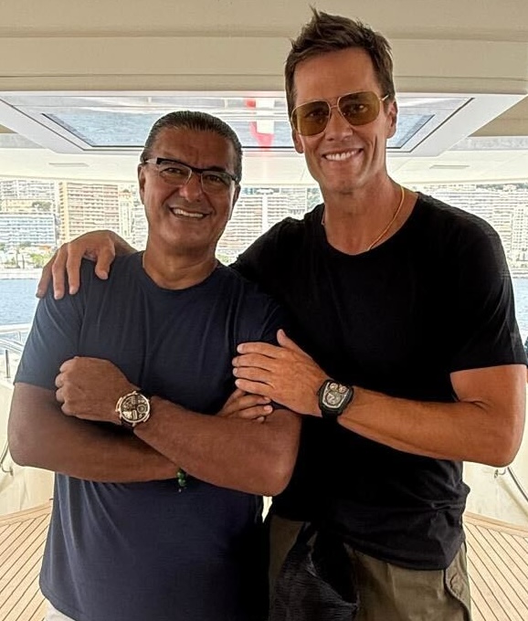 Two men stand side by side on a boat in Monaco, smiling at the camera. Both sport sunglasses and watches—one even wears the striking Jacob & Co. Twin Turbo Furious—while dressed in black and navy blue t-shirts.
