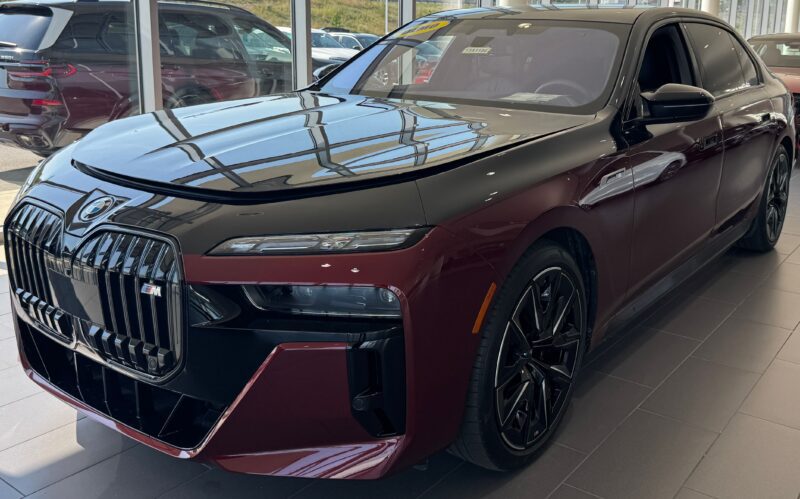 A maroon and black BMW sedan is displayed inside a showroom, featuring a large front grille and black alloy wheels—perfect for those seeking the best car leases on the latest models.