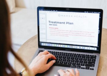 Person typing on a MacBook displaying a slide titled "Treatment Plan" with primary goals for a personalized health upgrade and improved energy.