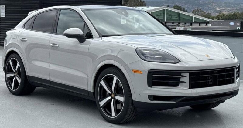 A white Porsche SUV, available with some of the best lease deals, is parked on a rooftop with mountains in the background.
