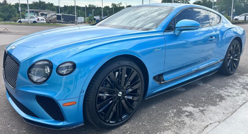 A blue Bentley Continental GT coupe with black wheels, parked in a lot on a cloudy day—an inspiring sight for anyone searching for the best car lease deals.