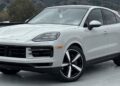A white Porsche SUV, available through the best car lease offers, is parked outdoors on a concrete surface with hills and trees in the background.