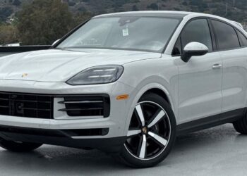 A white Porsche SUV, available through the best car lease offers, is parked outdoors on a concrete surface with hills and trees in the background.