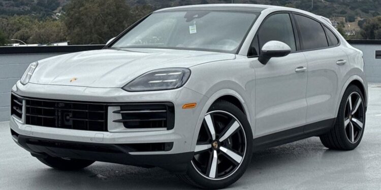A white Porsche SUV, available through the best car lease offers, is parked outdoors on a concrete surface with hills and trees in the background.