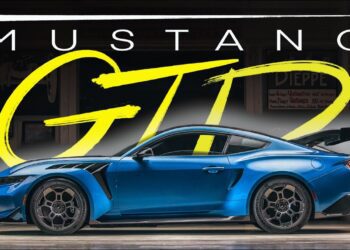 A blue Ford Mustang GTD parked indoors, viewed from the side, with bold text "MUSTANG GTD" displayed above the car—just like one Jay Leno might showcase in his legendary garage.
