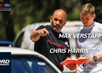 Chris Harris and Max Verstappen stand outdoors beside a Ford Mustang GTD; one points ahead while the other holds a red box. Text labels identify them, with Ford and Red Bull logos visible in the background.