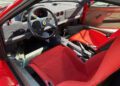 Interior view of a classic Ferrari F40 sports car featuring a black steering wheel with the Ferrari logo, red bucket seats, and a manual gear shifter—an iconic 1990 Ferrari now available at auction.