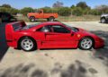 A red Ferrari F40 sports car, perfect for collectors looking to buy at auction, is parked on a concrete driveway with an orange pickup truck and trees in the background.