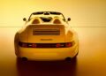 Rear view of a yellow Porsche Speedster convertible, a stunning example of Porsche exclusive craftsmanship, photographed against a warm yellow background.