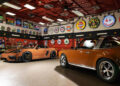 A garage featuring two Sepia Brown Porsches, vintage automotive signs on the walls, a red ceiling, tool cabinets, and various car memorabilia—the perfect haven for any Porsche collector.