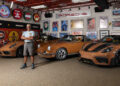 A Porsche collector stands in a garage with three Sepia Brown Porsches, surrounded by bicycle wheels and vintage automotive signs and posters on the walls.