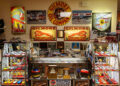 Display of vintage automobilia, including Gilmore Oil signs, model race cars, classic Porsche trophies, plaques, and various racing memorabilia—all thoughtfully arranged on shelves and walls.