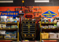 Organized garage workspace with labeled storage bins, cleaning supplies, tools on wall mounts, Firestone and Goodyear signs on an orange and black wall—perfect for a Porsche collector or anyone passionate about sepia brown Porsches.