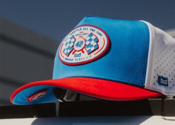A blue, white, and red Odyssey Hat by melin with a round NASCAR-inspired racing patch on the front, featuring checkered flags and the number 42, resting on a white surface.