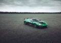 A green and black Rimac Nevera, the fastest EV that’s breaking electric car records, is parked on an empty, expansive asphalt lot under a cloudy sky.