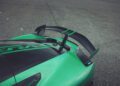 Close-up of the Rimac Nevera, one of the fastest EVs, showcasing its green rear spoiler with black and green detailing, parked on a gray asphalt surface.