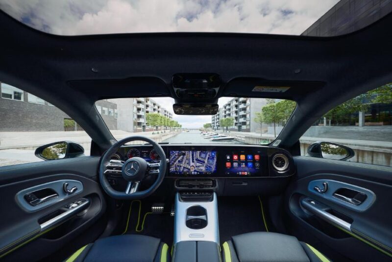 Interior view of a modern Mercedes-Benz car featuring the steering wheel, digital dashboard, and touchscreen with navigation—parked in an urban setting, where Mercedes Benz becomes first automaker to natively integrate Microsoft Teams 365 Copilot and Intune.