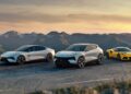 Three modern sports cars—two white and one yellow—are parked on a mountain road at sunset, evoking the spirit of Lotus to honor F1 legends Senna and Clark at Goodwood, with hills and trees visible in the background.
