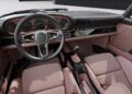 The image shows the interior of a classic-style car with a leather-wrapped steering wheel, analog gauges, manual gear shift, and brown-pink upholstery—much like the reimagined Porsche 911 Carrera Coupes unveiled by a California-based singer at Goodwood.