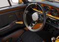 Close-up view of a classic car interior in a California-Based Singer reimagined Porsche 911 Carrera Coupe, featuring a three-spoke steering wheel, analog gauges, manual gear shift, and striking black and yellow trim.
