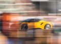 A yellow sports car speeds past blurred surroundings, its motion echoing the excitement as Lotus honors F1 legends Senna and Clark at Goodwood, with the background melting into indistinct details.