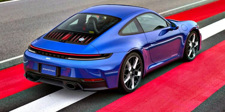 A blue Limited-Run 911 Carrera T Club Coupe sports car is parked on a red and white striped section of a racetrack, viewed from the rear left side.