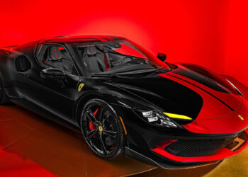A black Ferrari sports car with yellow accents is displayed under bright red lighting at Ferrari of San Antonio, highlighting its sleek and aerodynamic Italian supercar design.