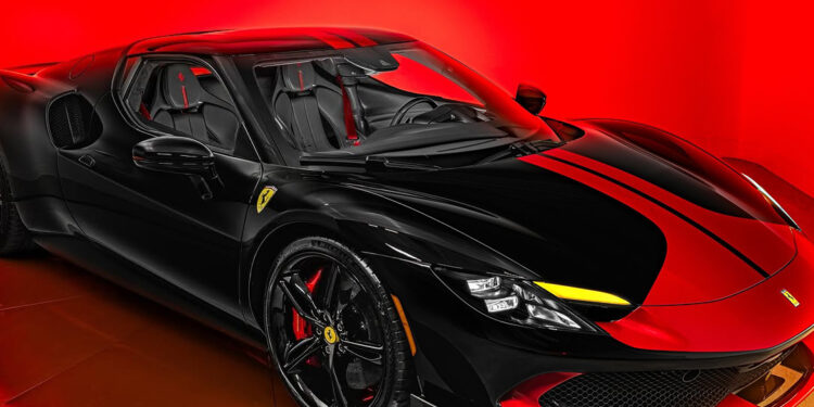 A black Ferrari sports car with yellow accents is displayed under bright red lighting at Ferrari of San Antonio, highlighting its sleek and aerodynamic Italian supercar design.