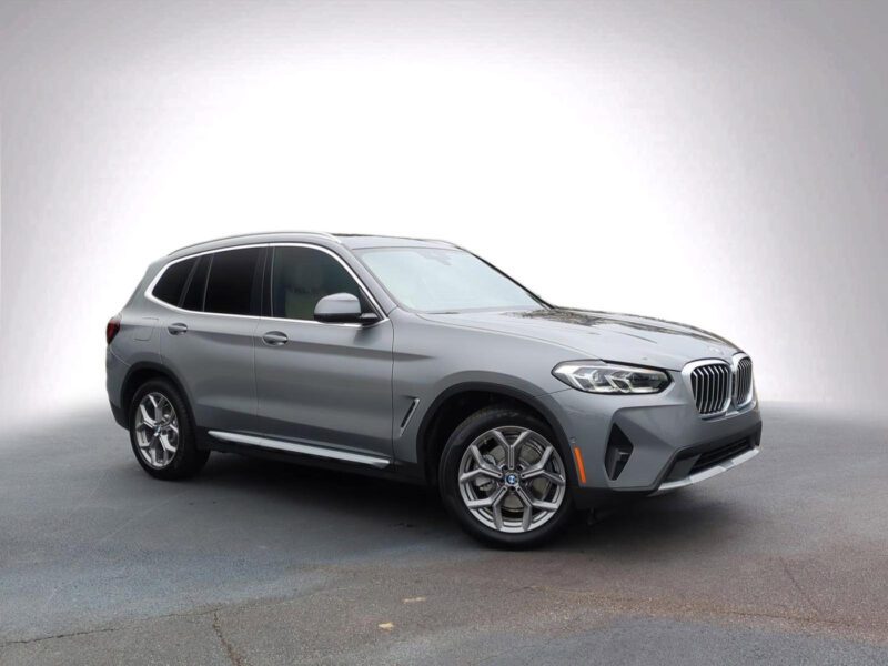 A silver BMW SUV is parked on a plain, textured surface with a white gradient background, an ideal choice for those seeking the best car lease deals.