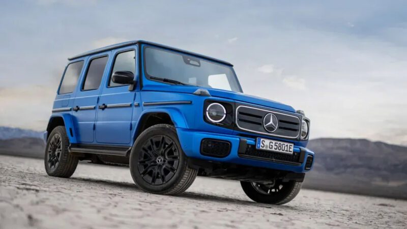 A blue Mercedes-Benz G-Class SUV, perfect for those seeking the best lease deals, is parked on a dry, rocky terrain with mountains and a cloudy sky in the background.