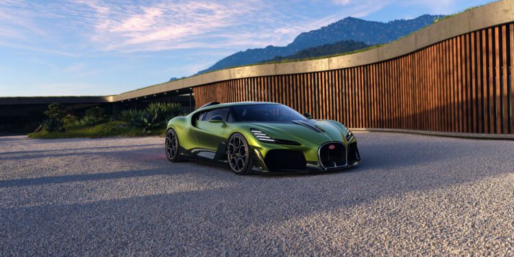 A green Bugatti sports car is parked on a gravel driveway in front of a modern wooden building with mountains in the background.