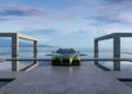 A green sports car is parked on a modern, geometric platform surrounded by reflecting pools, with mountains and a lake in the background under a partly cloudy sky.