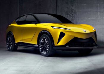 A yellow all-electric SUV with black accents is parked indoors against a gray concrete wall, showcasing sleek lines and modern design features inspired by Monterey style and Acura RSX influences.