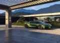 A green Bugatti sports car with a powerful W16 engine is parked outside a modern house with large glass windows, surrounded by mountains and lush greenery.