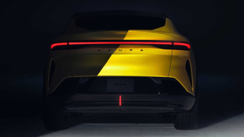 A yellow Acura RSX is shown from the rear under partial lighting at Monterey, highlighting its sleek taillight strip and Acura lettering on the trunk.