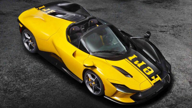 A yellow and black sports car with an open top, two seats, and "FERRARI" written across the hood, parked on a dark textured surface—an icon fit for the 10 Most Expensive Cars To Sell At 2025 Monterey Car Week Auctions.
