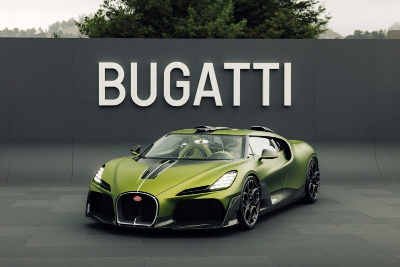 A green Bugatti Brouillard W16 sports car is parked in front of a large wall with the word "BUGATTI" displayed in white letters, capturing the spirit of The Quail.