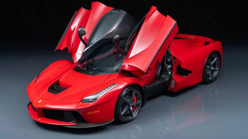 A red sports car with butterfly doors open, parked on a shiny surface and viewed from an elevated front angle, could easily be featured among the 10 Most Expensive Cars To Sell At 2025 Monterey Car Week Auctions.