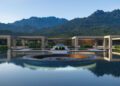 Modern luxury villa complex with a central pool and a stunning Bugatti W16 parked in the middle, surrounded by mountains and greenery under a clear sky.