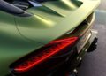 Close-up of the rear end of a green Bugatti sports car with illuminated red tail lights, carbon fiber accents, and dual exhausts, parked next to a reflective water surface—its W16 power hinted in every curve.