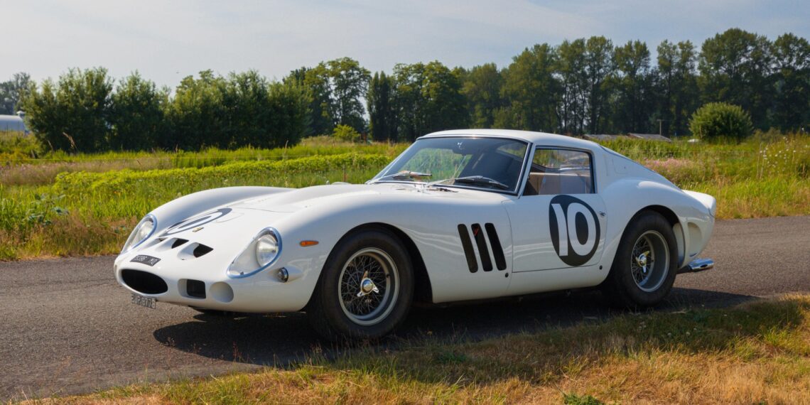 A factory white Ferrari 250 GTO with the number 10 on the door is parked on a rural road, surrounded by grass and trees under a clear sky—a stunning sight reminiscent of a Mecum Kissimmee Auction classic.