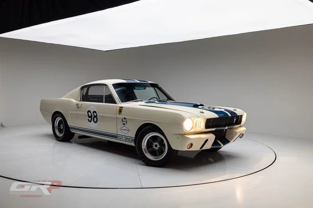 A classic white Ford Mustang race car with blue racing stripes and number 98 on the door, parked in a well-lit white studio—an icon of high-performance history among classic muscle cars.
