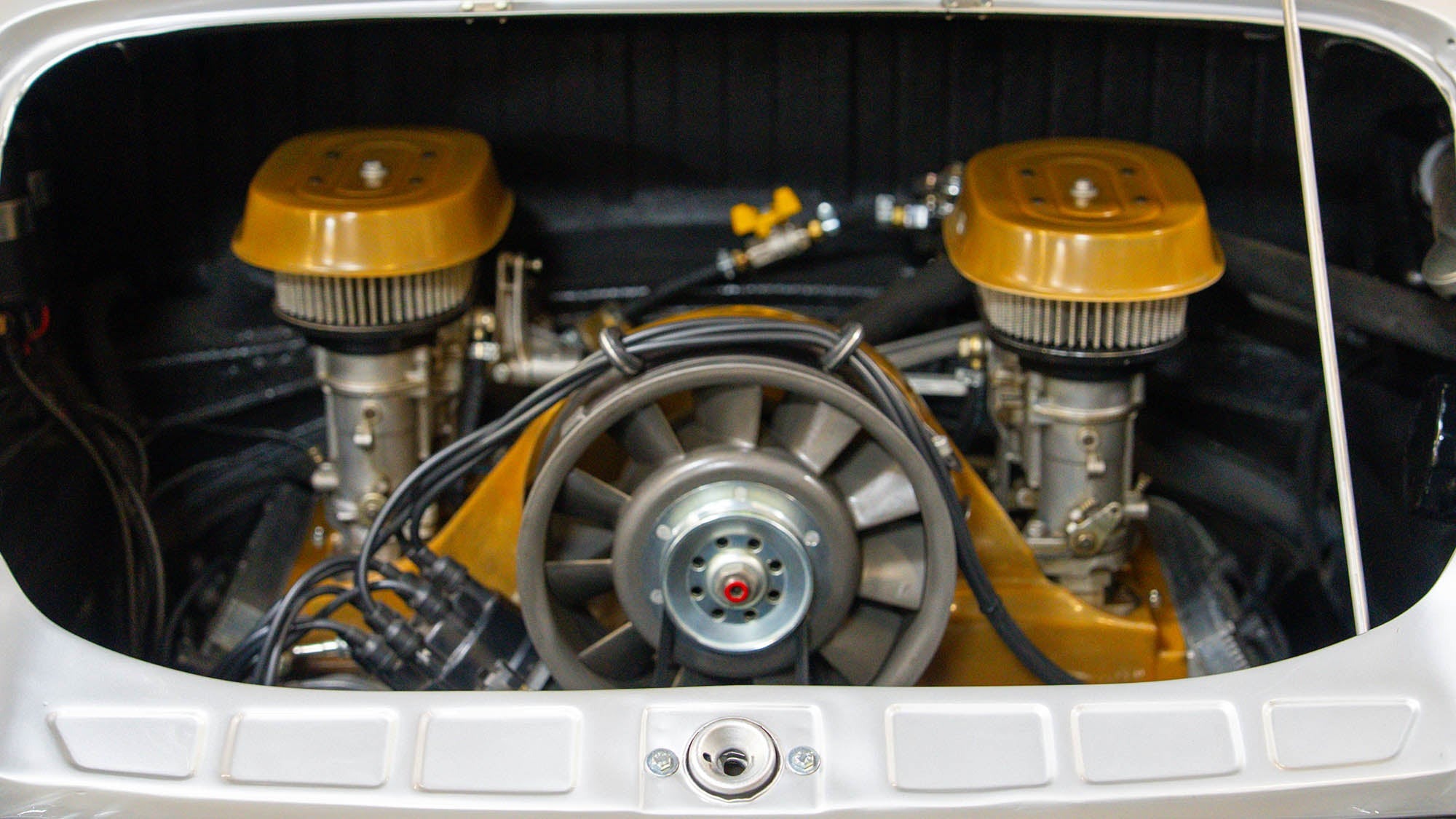 Close-up view of a Porsche 912 engine compartment, inspired by the 1968 Prototype, featuring dual carburetors and a central cooling fan in true Petrolicious style.