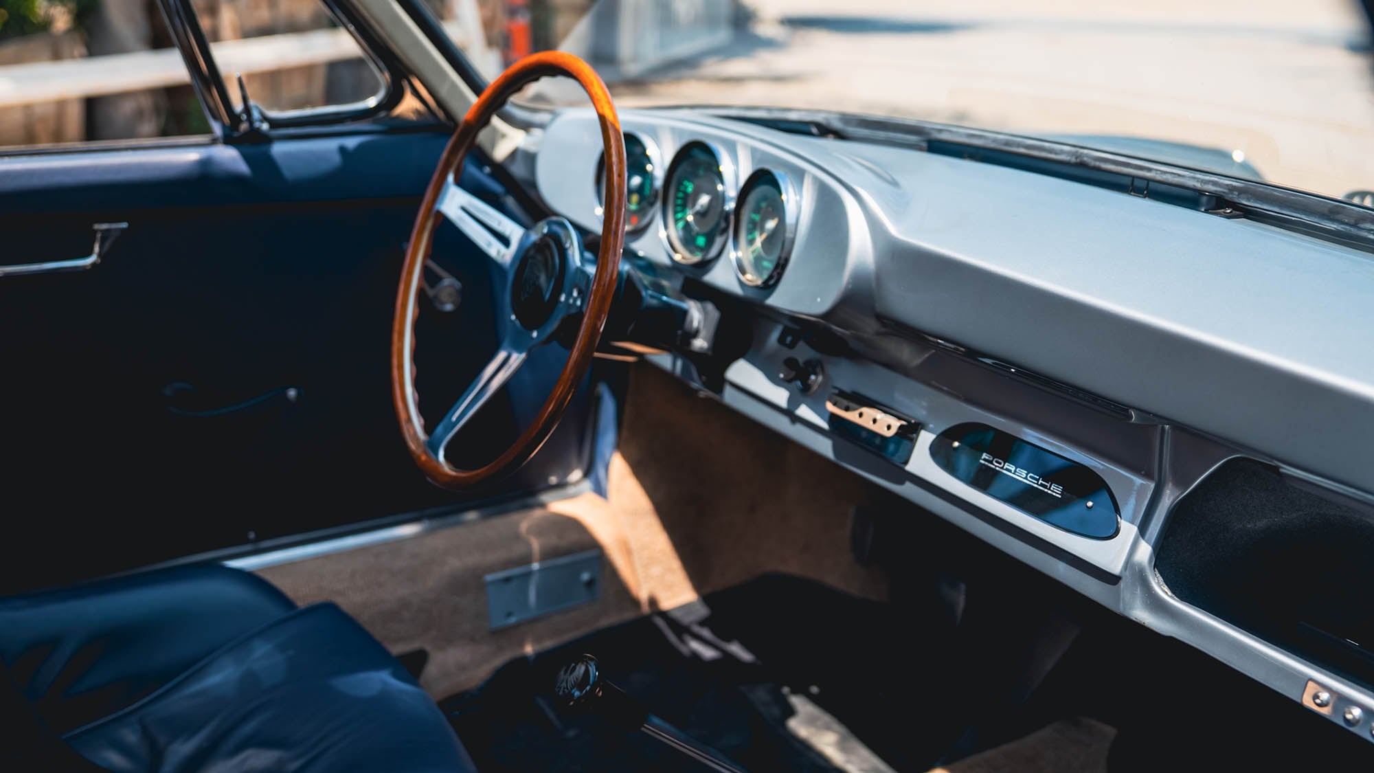 Interior of a classic Porsche 912 showing a wooden steering wheel, vintage dashboard with round gauges, and dark seating—a scene worthy of Petrolicious enthusiasts.