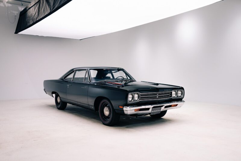 A vintage black two-door Plymouth Road Runner car is displayed in a well-lit, white studio—one of the highlights inspired by 2025 Bonhams Monterey: 10 Must-See Cars Crossing the Block at The Quail.